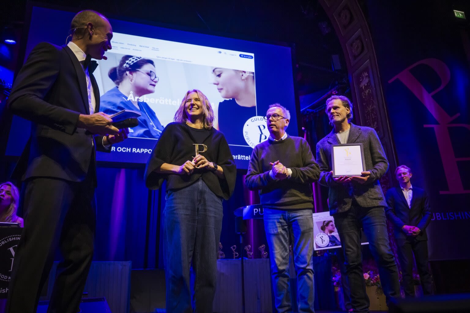 Three people accept a prize on stage.