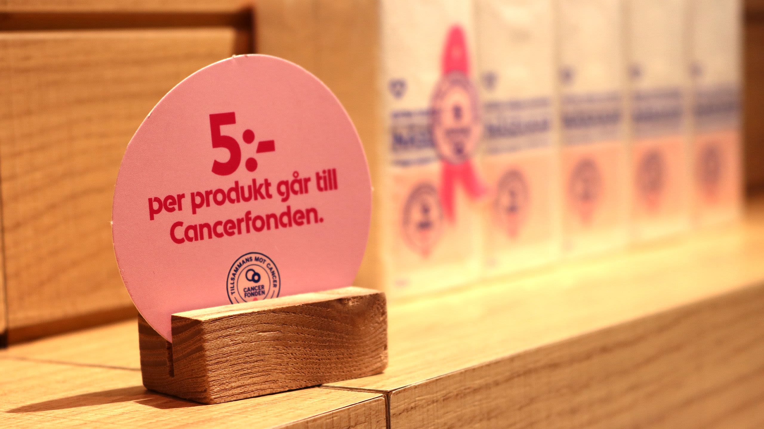 A small sign on a shop counter reads 5 per produkt gar till Cancerfonden.