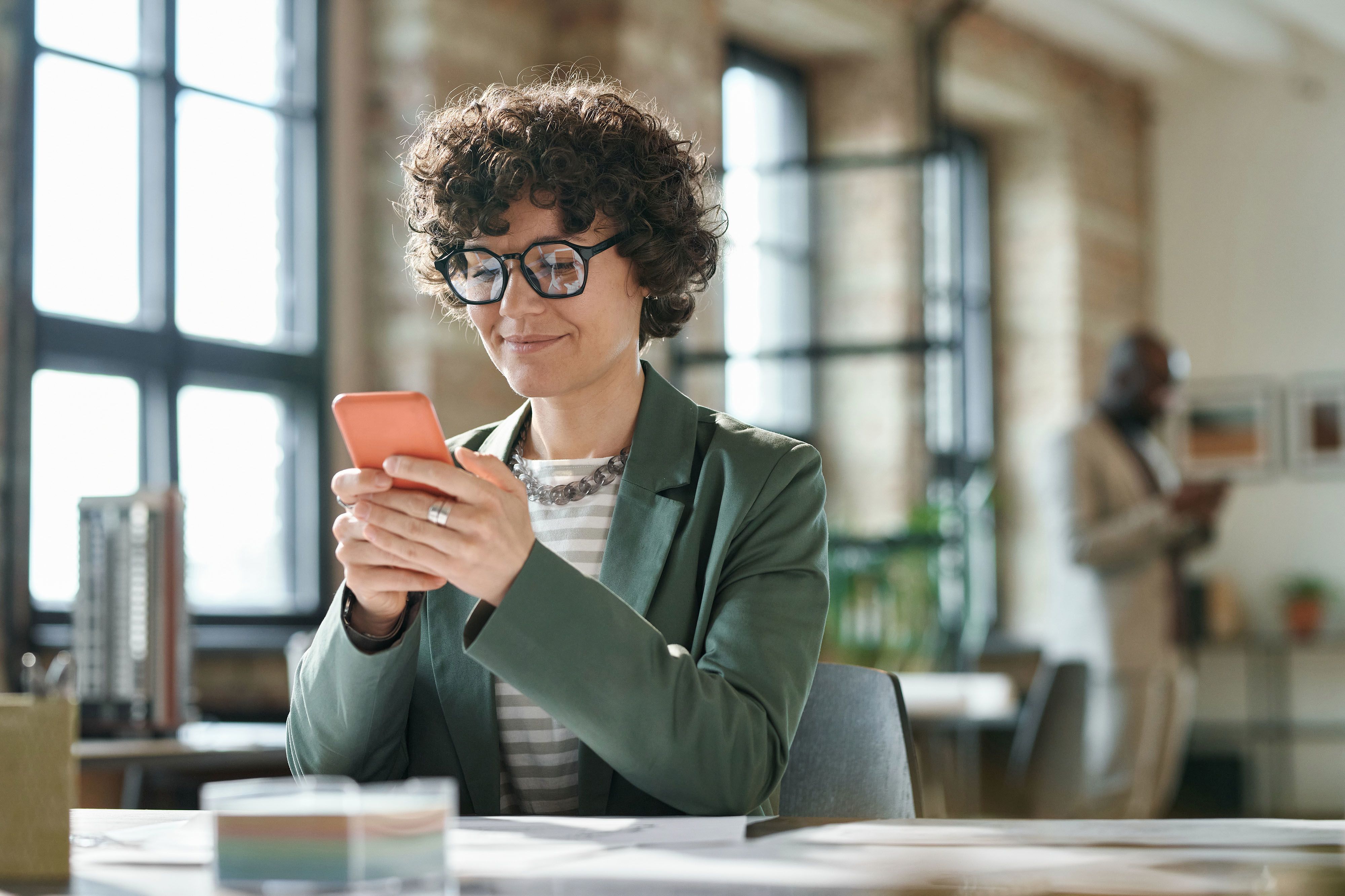 A person sitting at a desk. They are smiling and looking at their smartphone.