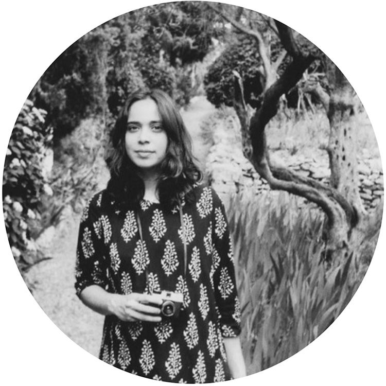 A black and white images of a person with a forest in the background, the are holding a camera.