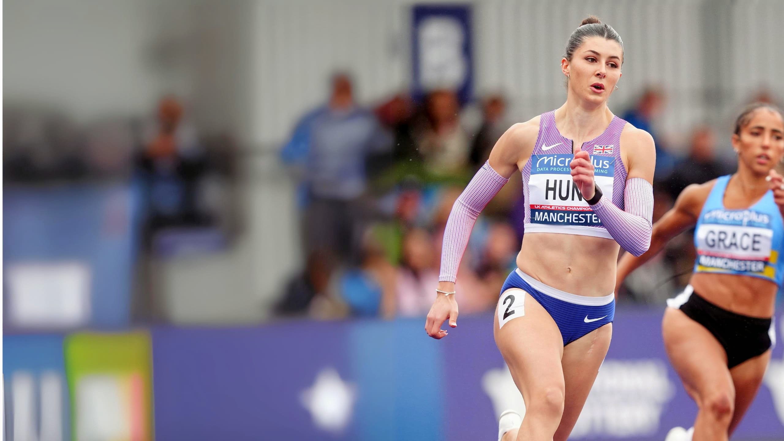 A woman with white skin and brown hair in racetrack gear sprinting..