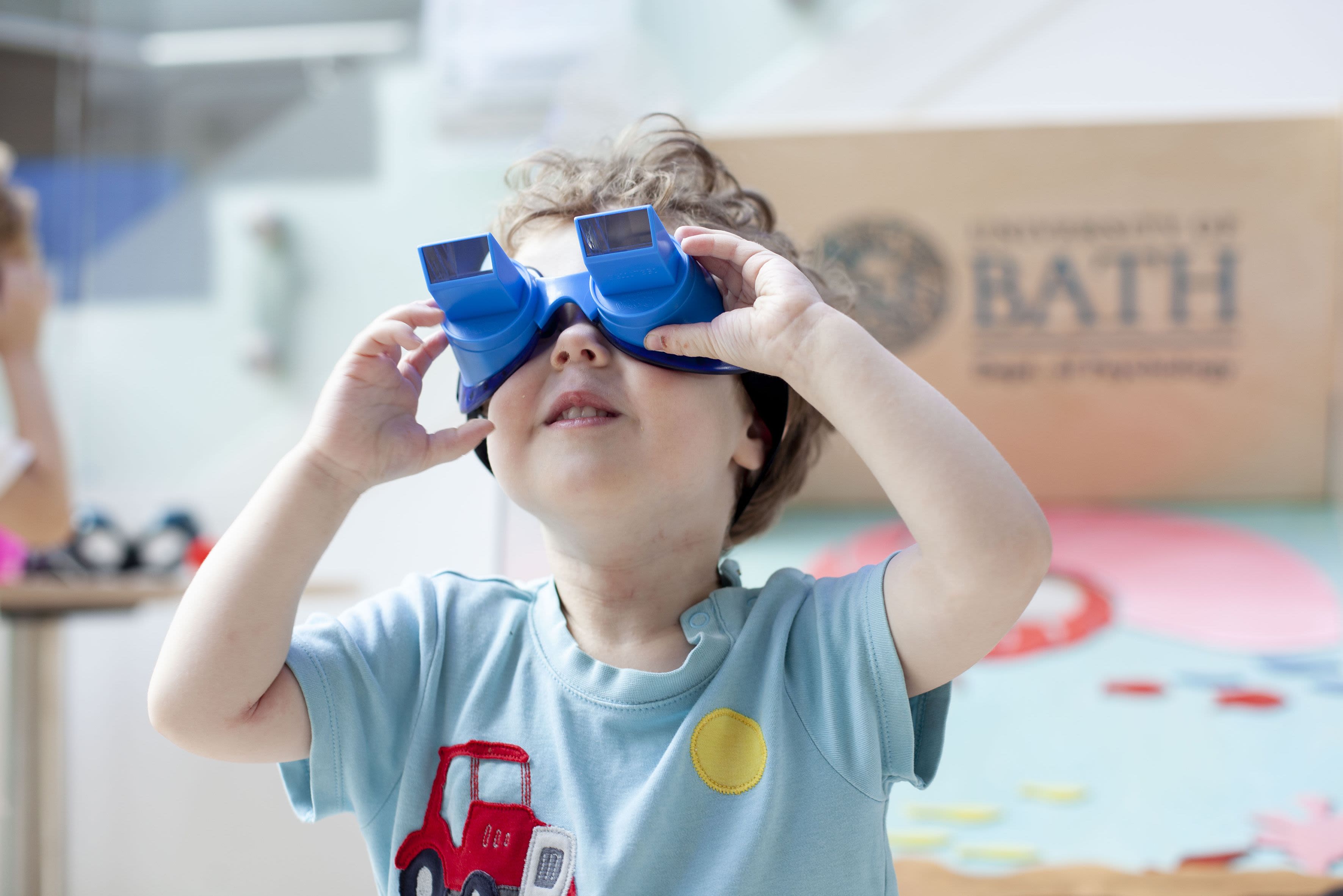 A young child with white skin looks through blue toy goggles.