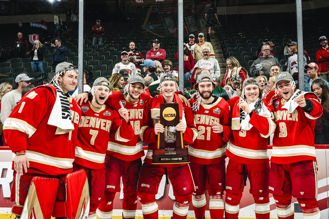 An ice hockey team in red uniforms celebrates with a trophy.