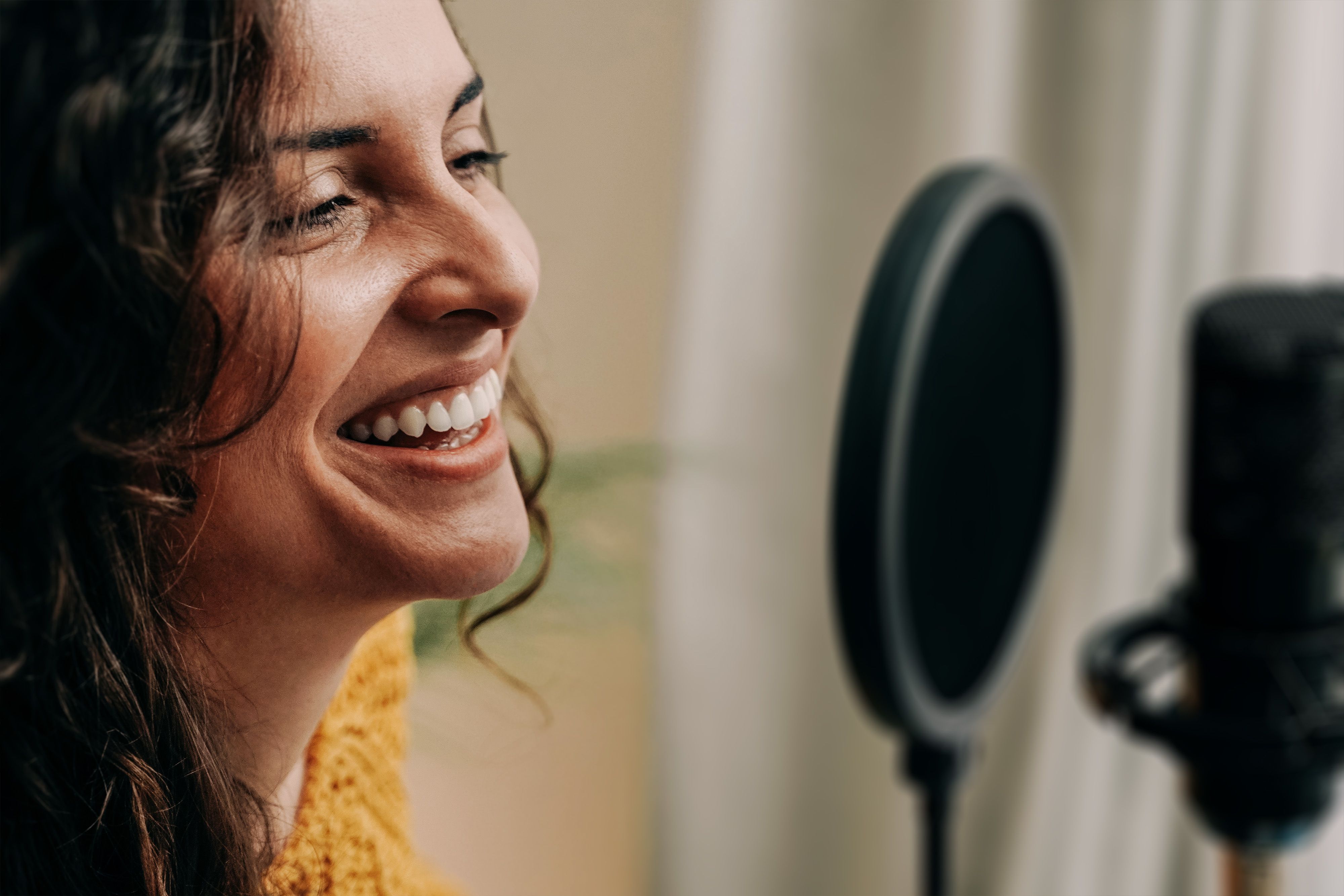 A person smiling while speaking into a podcasting microphone.
