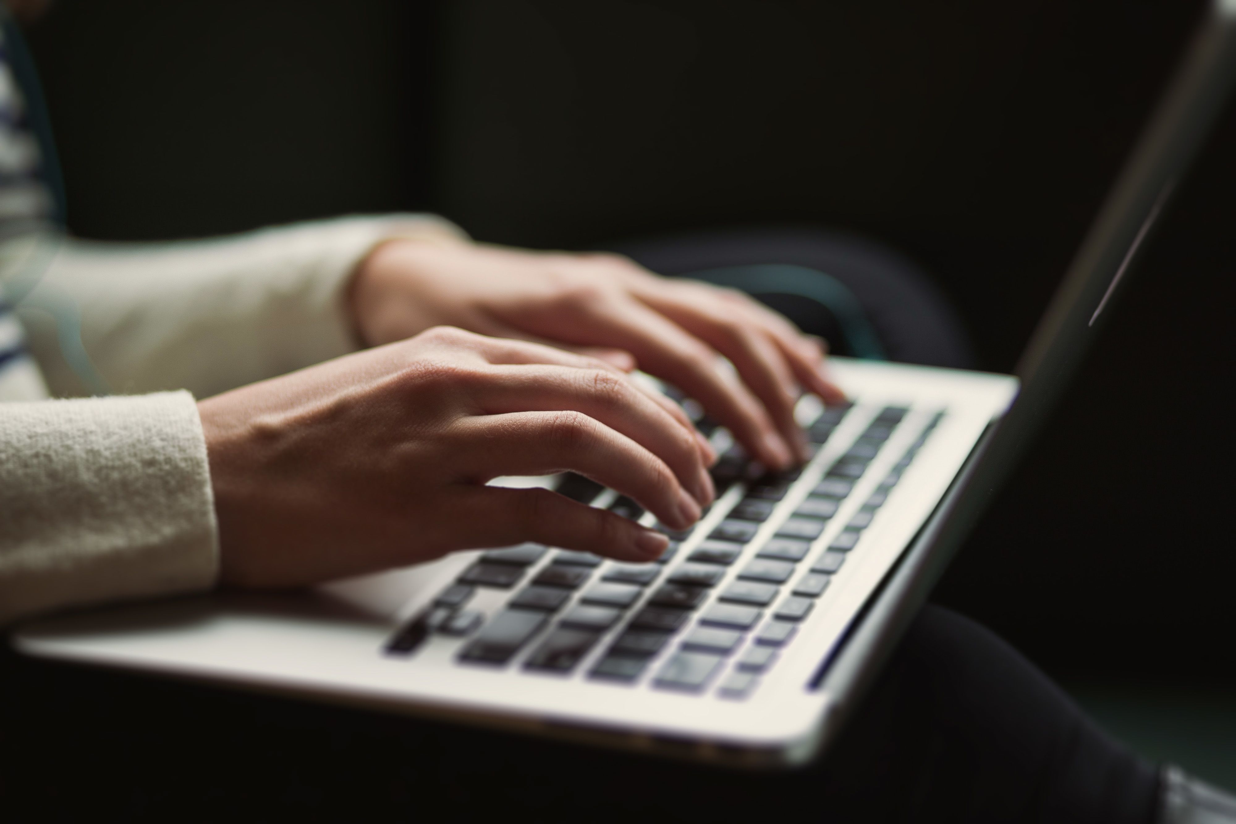 A close up image of a person's hands typing on a laptop keyboard.