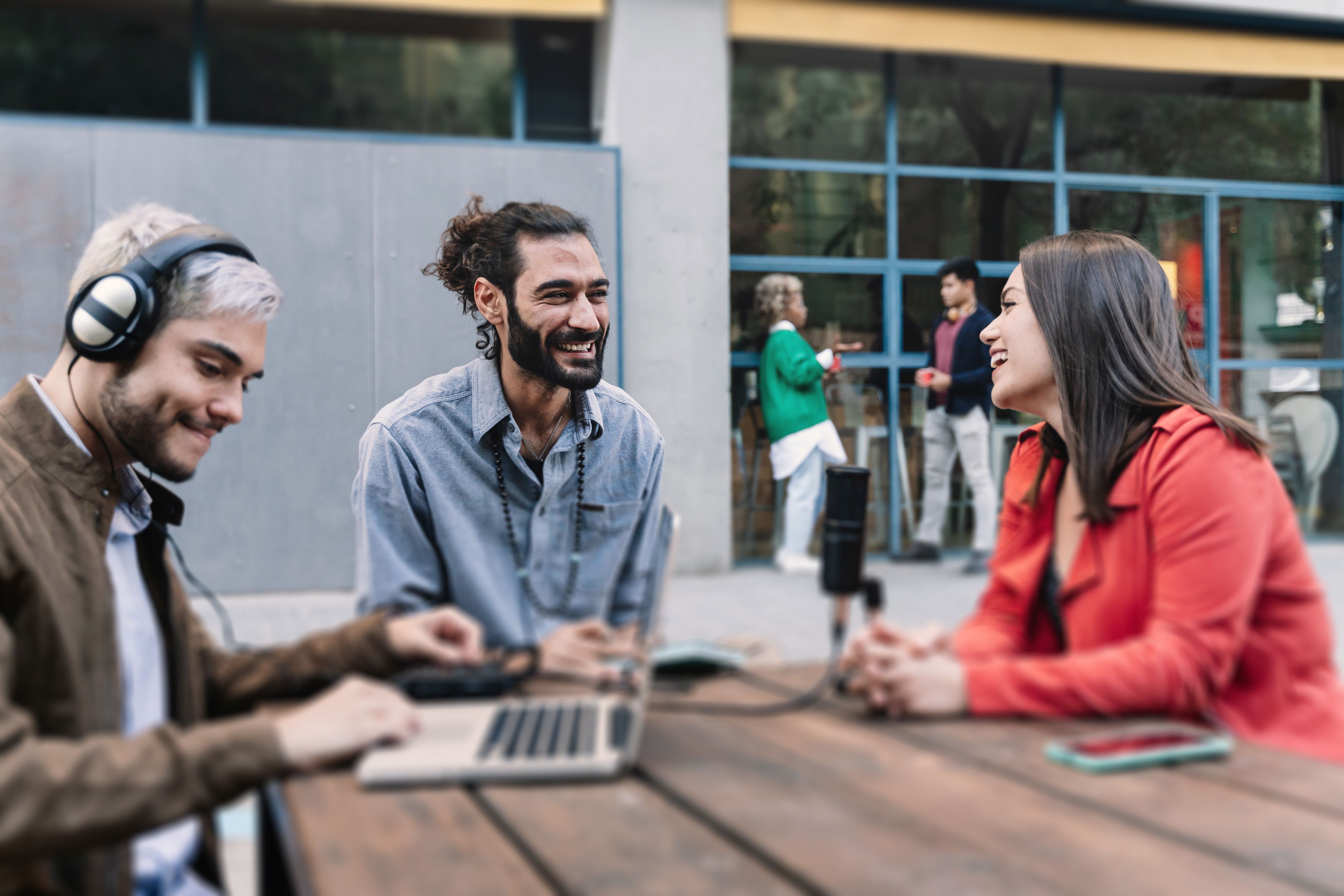 Three smiling people sitting around a table with laptops.