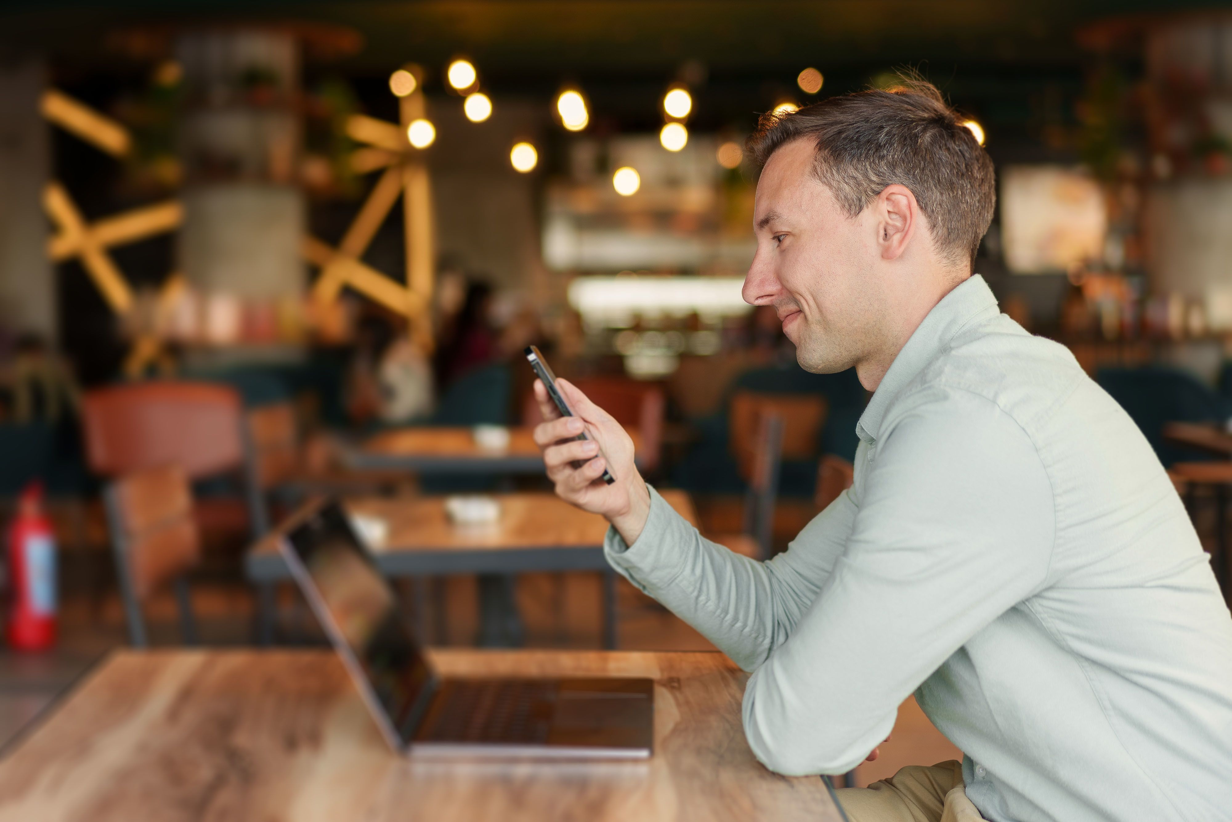A person smiling while reading his phone at a cafe.