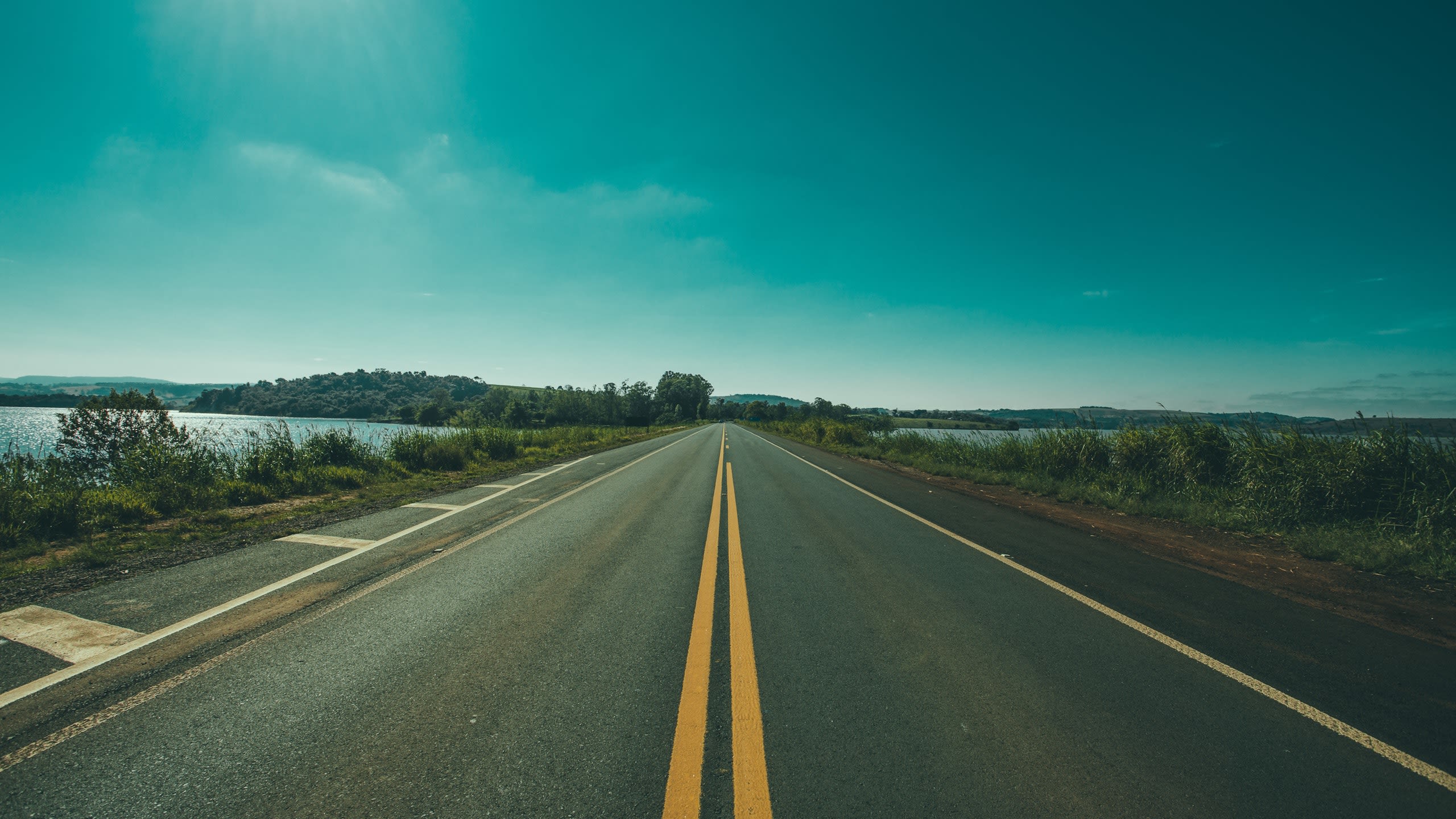 A long straight road framed by grass with hills in the background 