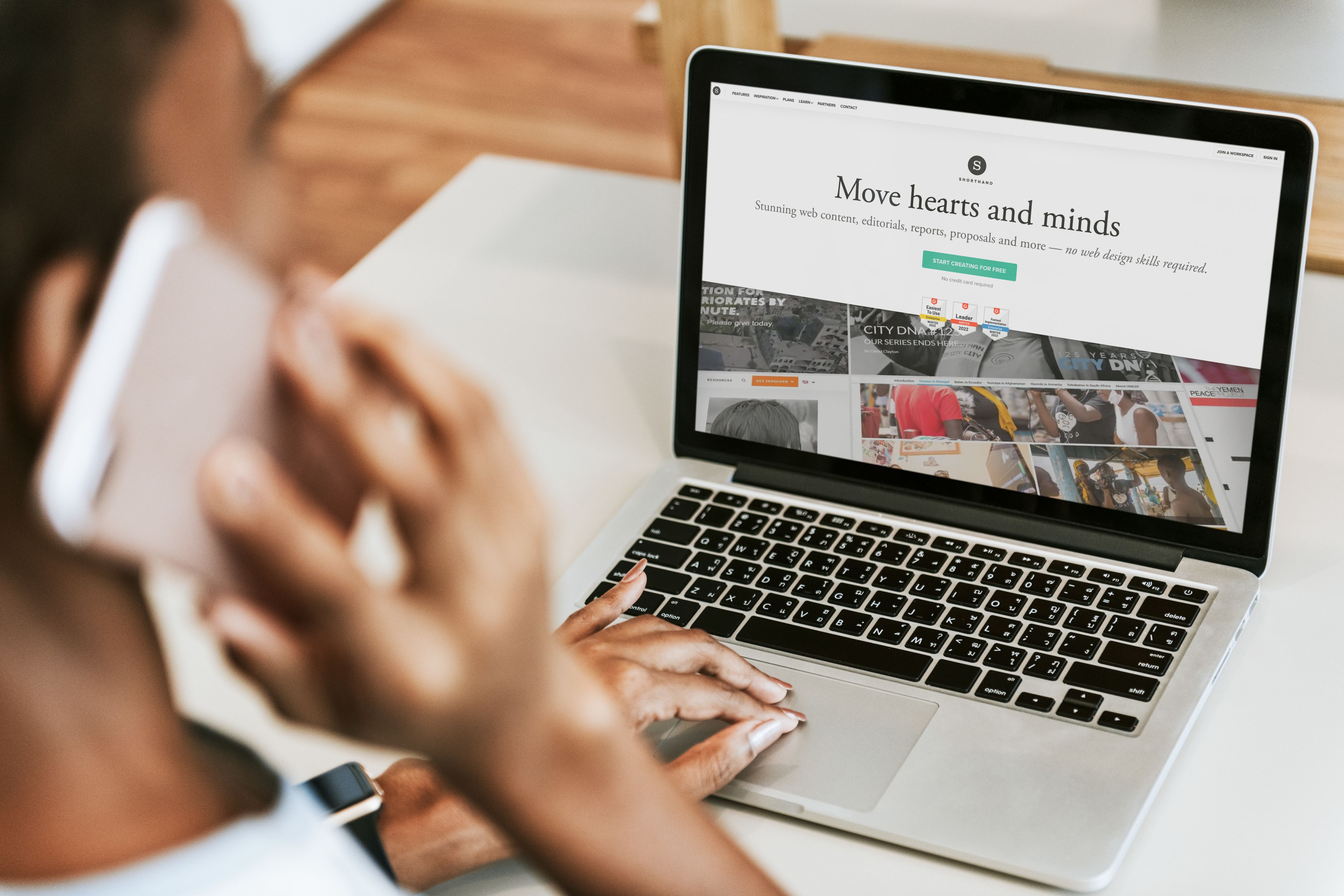 A person working on a laptop and talking on a smartphone. They're looking at the Shorthand website.