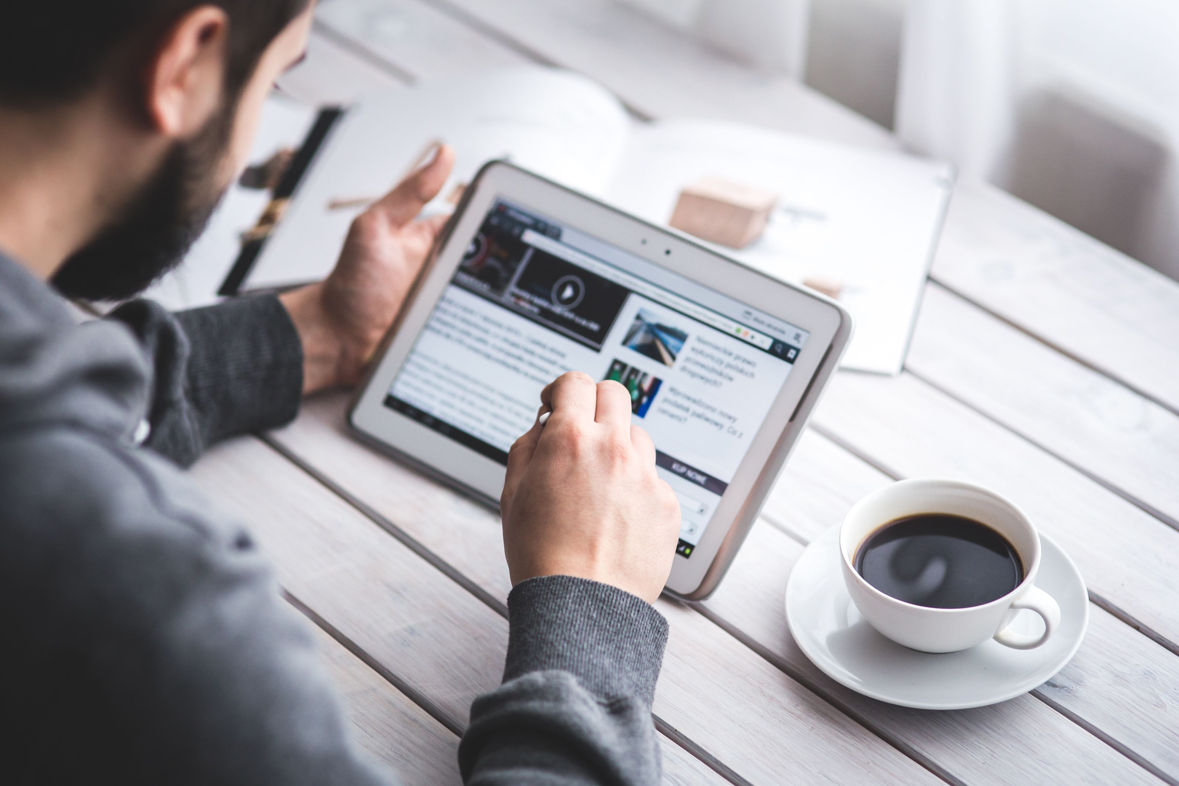 A person sitting at a table with a cup of coffee looking at a tablet.