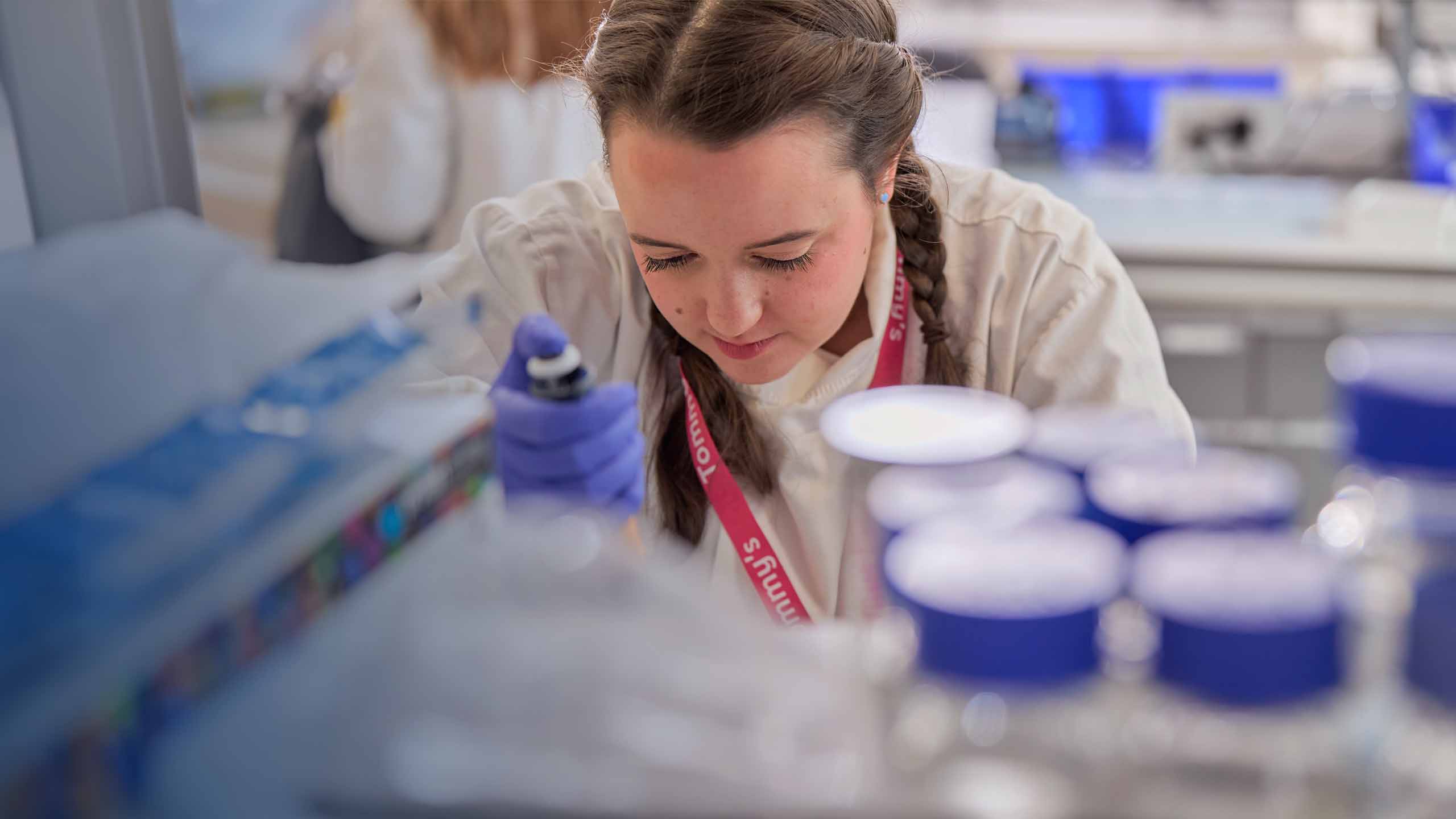A woman with white skin and dark hair pipes substance in a laboratory.