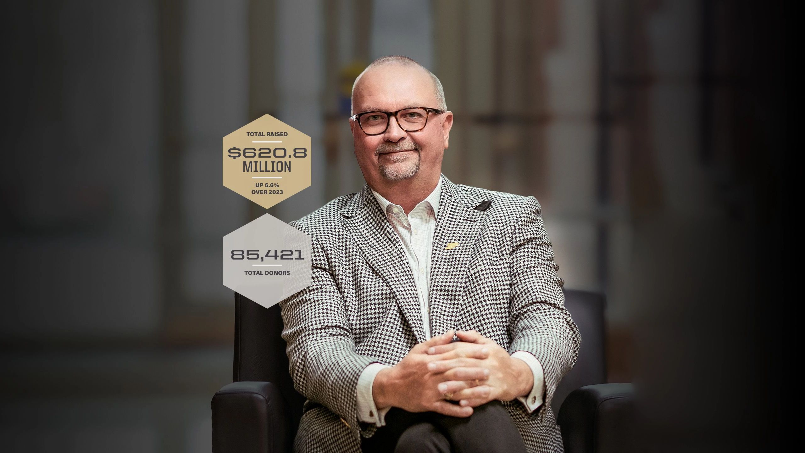 A white man with grey hair sits with his hands on his knees.