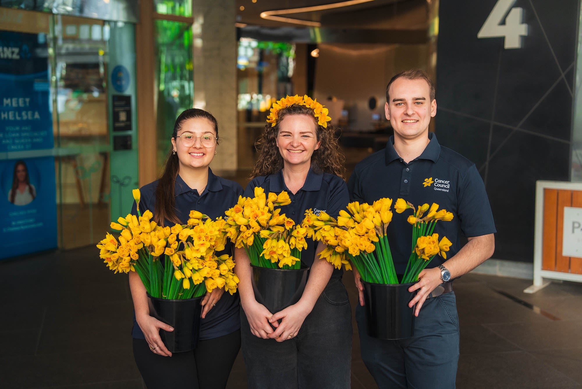 Two women and a man holding yellow flowers in buckets.