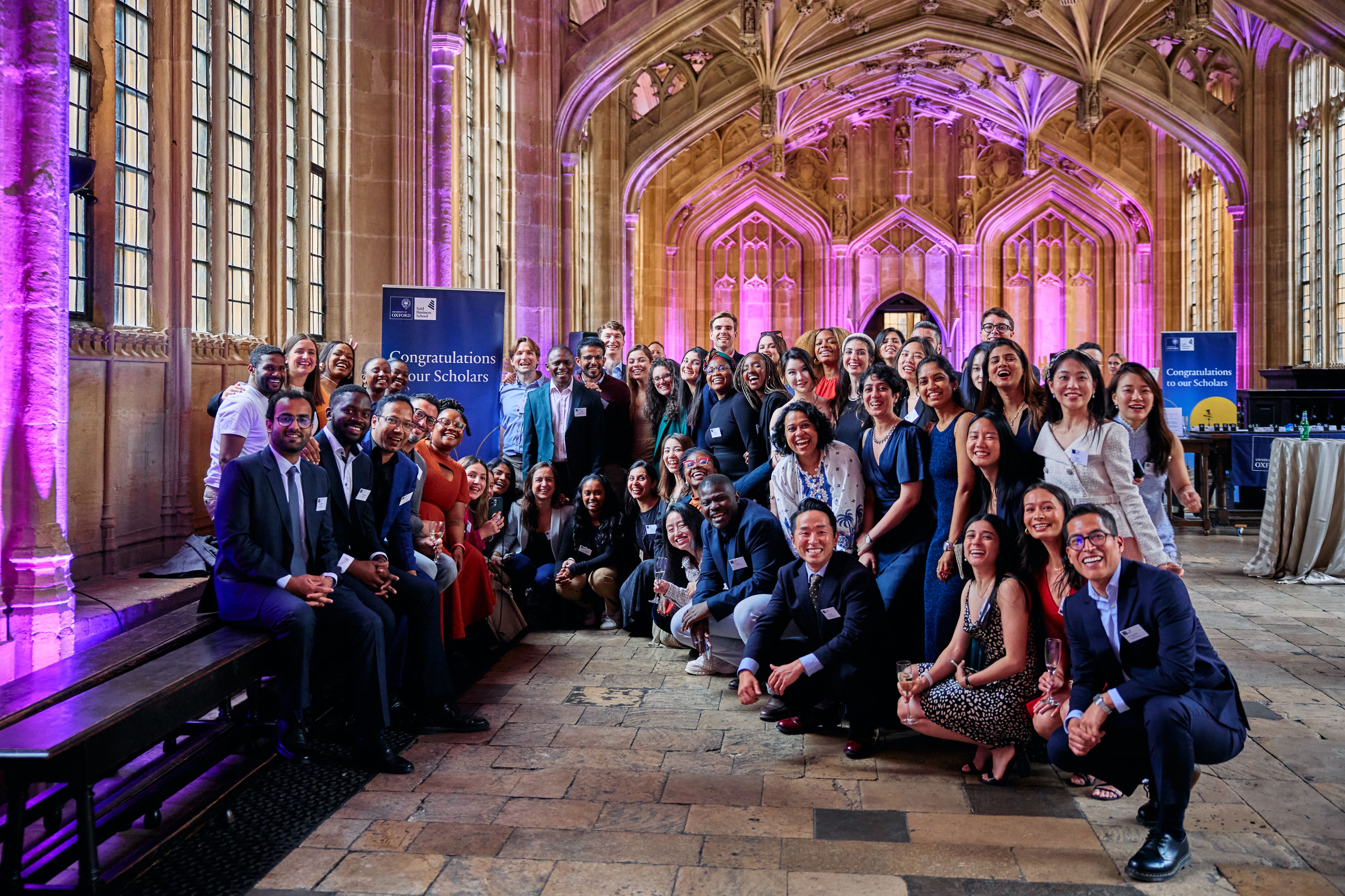 A large group of students poses for a group photo in a university interior.