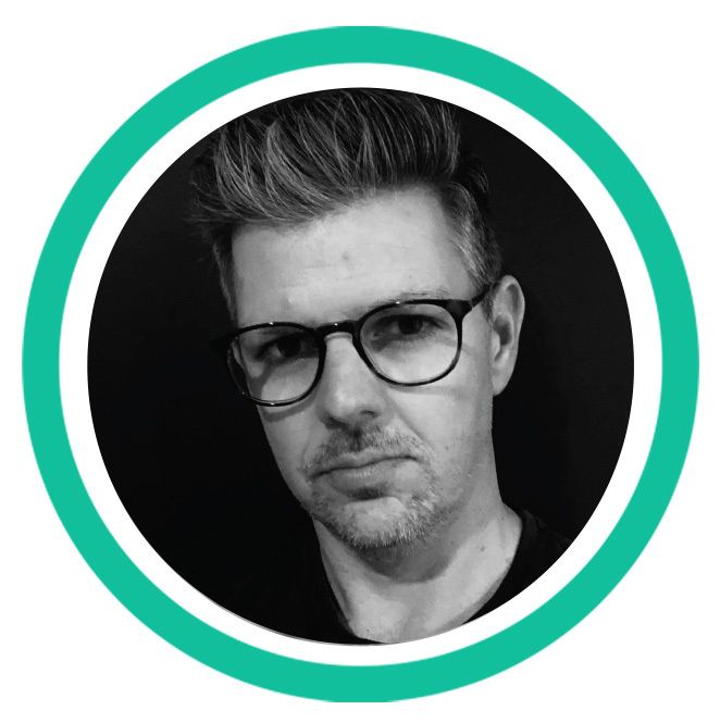 A black and white headshot of a man with black-framed glasses and short dark hair. 