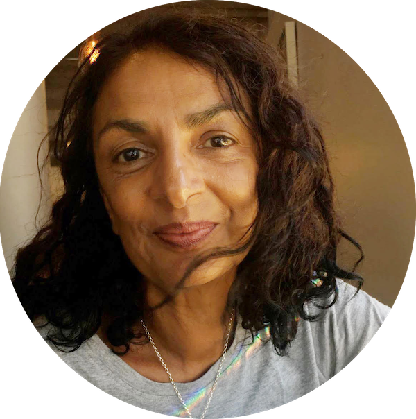 An older Indian woman with dark brown, shoulder-length hair, smiling directly at the camera