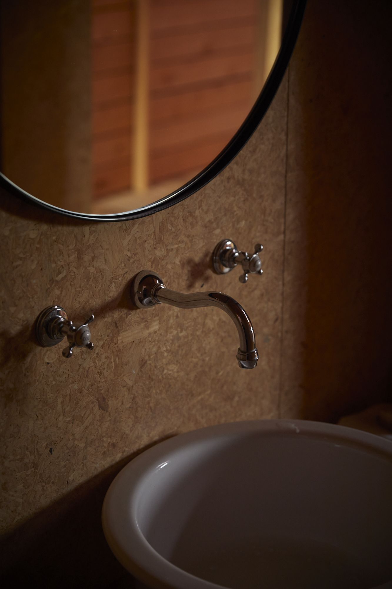 A tap and a mirror on wooden wall.