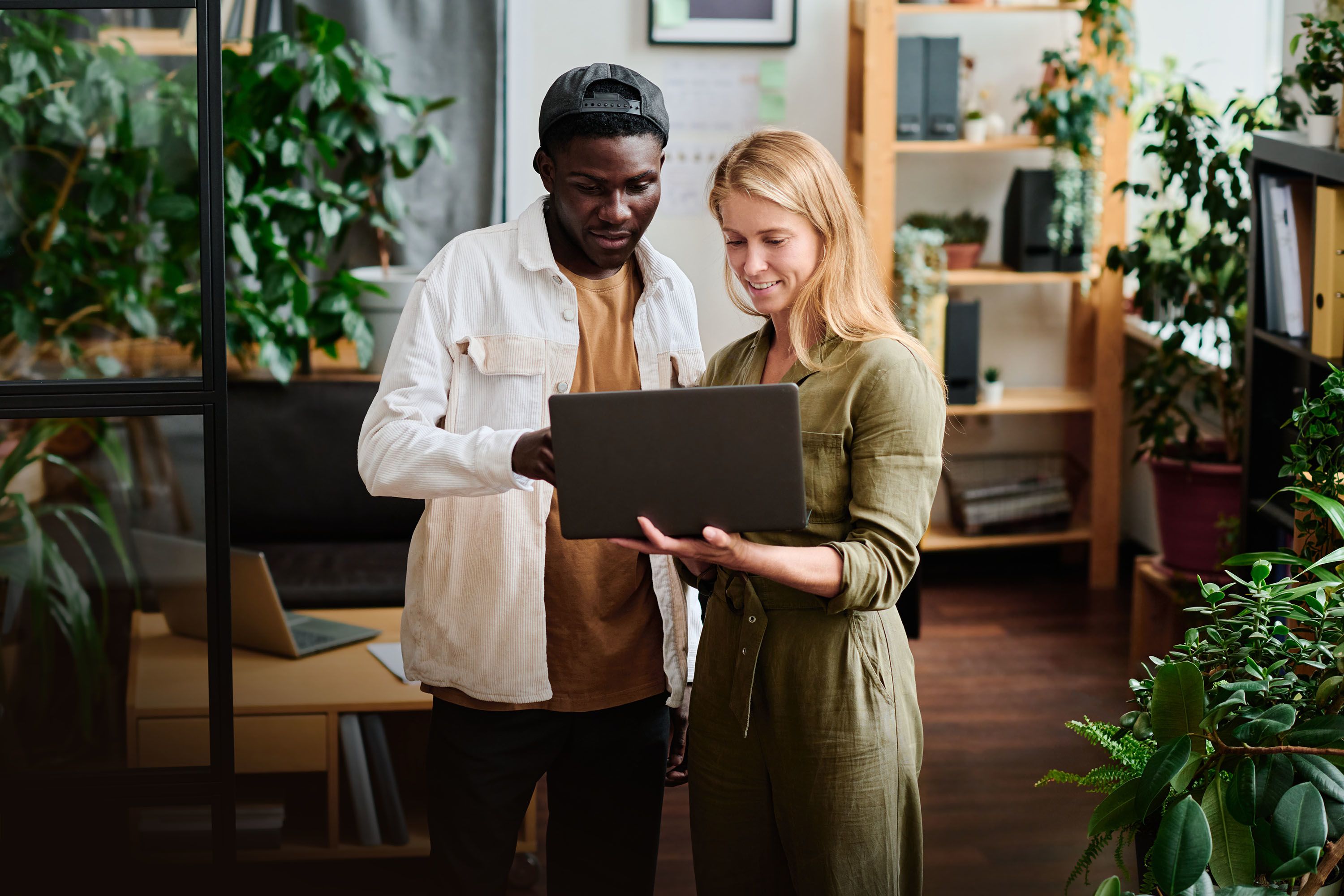 Two people standing in an office looking at a laptop with interested expressions.